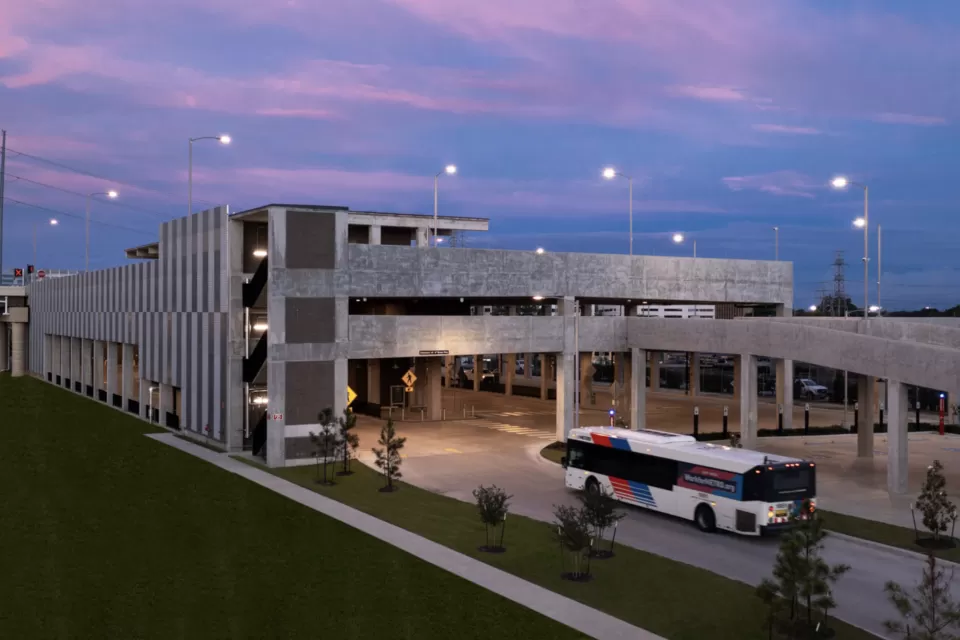 View of Westpark/Lower Uptown transit center in Houston with bus exiting three-story garage vuilding and purple sunset sky in background